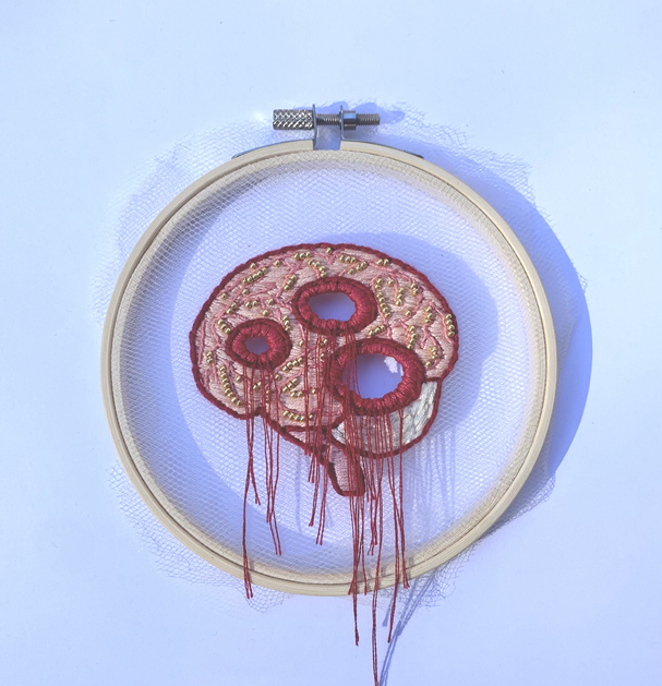 embroidered art of a pink brain with red holes. there are red strings coming out of the holes