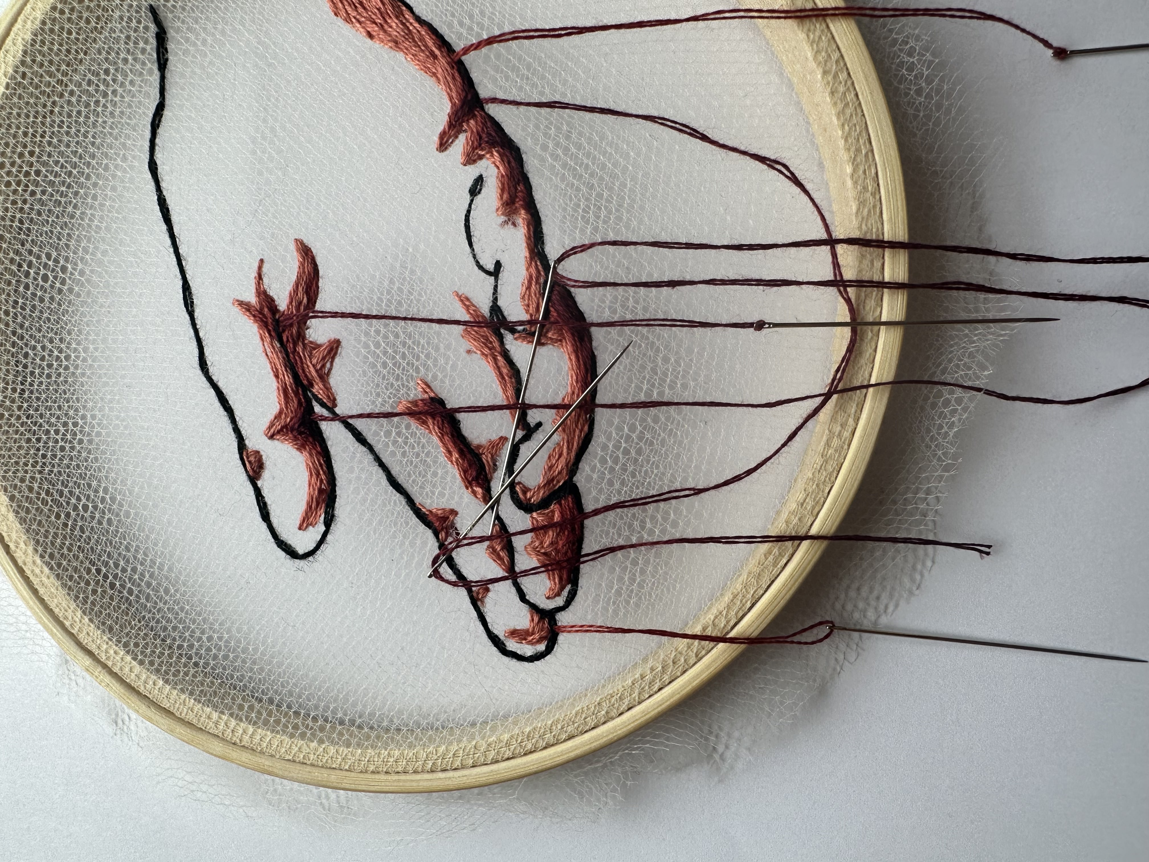 embroidered hand with three needles poking out of it