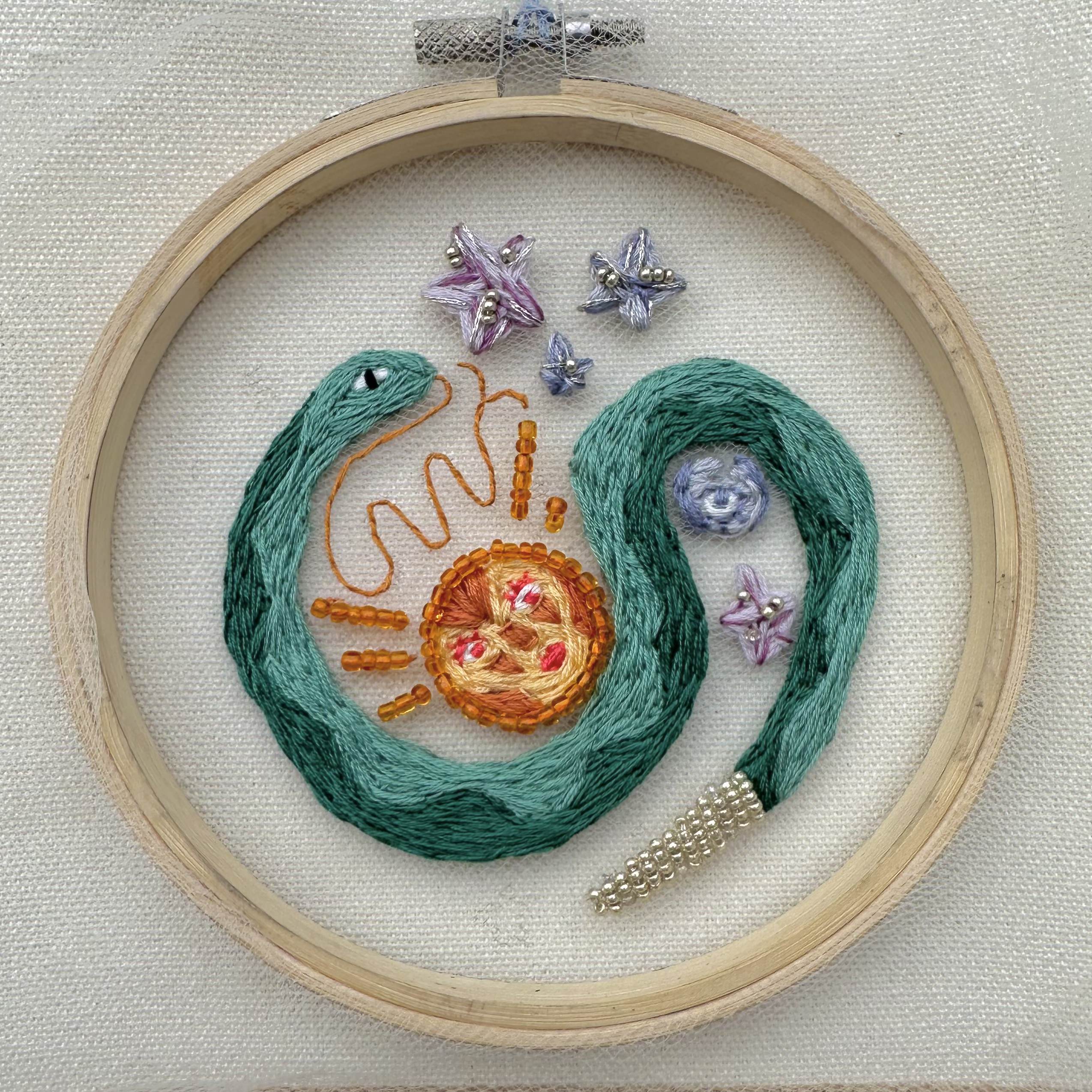 embroidered art of a turquoise snake with stars and a sun in the background